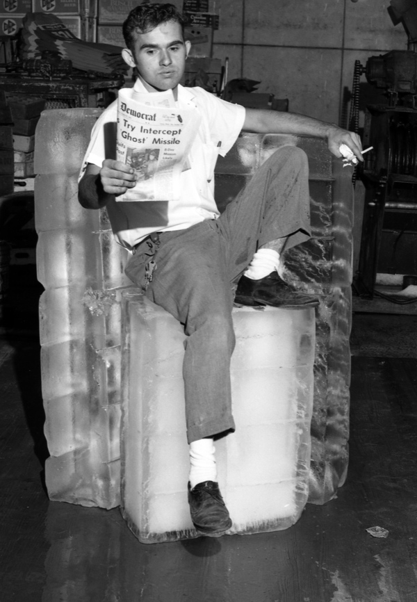 Employee James McCamon of the Middle Florida Ice Company cools off by reading the Tallahassee Democrat while sitting on a block of ice (1965).