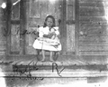 A little girl holding her doll on the porch.
