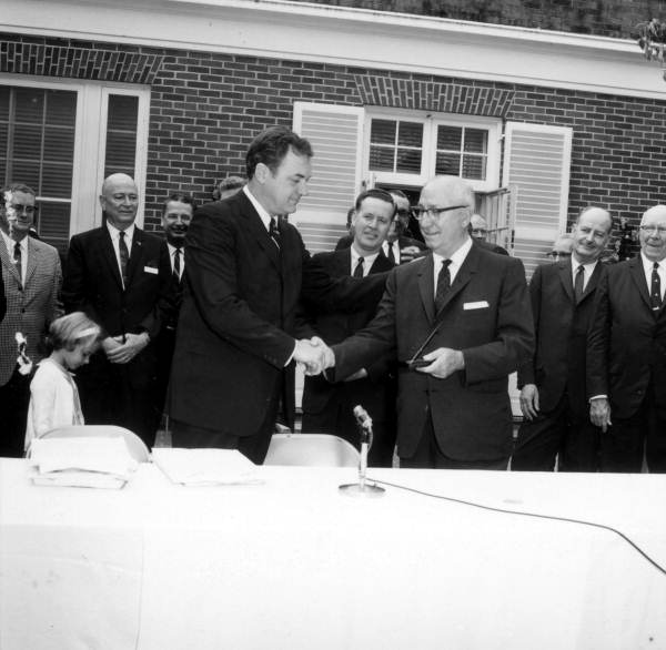 Governor Claude Kirk (left) shakes hands with Roy Disney (right) after signing new legislation facilitating the development of Walt Disney World (May 12, 1967).