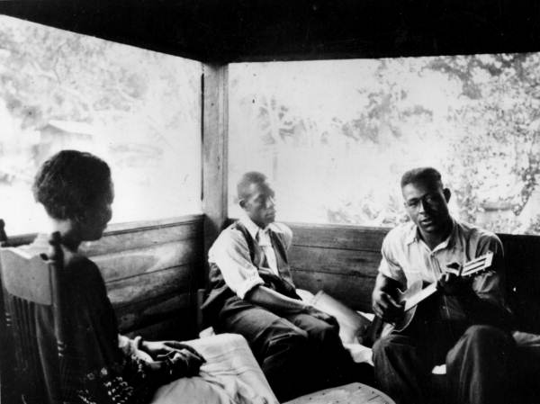 Gabriel Brown playing guitar as Rochelle French and Zora Neale Hurston listen- Eatonville, Florida