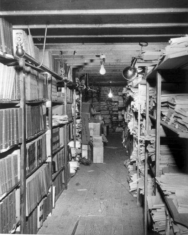 A view of the State Library’s storage area in the basement of the Old Capitol in 1947. Before the Department of State built a designated repository in the 1970s, the library’s collections were kept on different floors and wings of the capitol. Though archival best practices were not well-established at the time of this photograph, modern professional archivists follow a strict set of guidelines to ensure the longevity of their collections. Because of moisture’s deteriorative impact on paper, damp basements are not considered acceptable library and archive storage spaces. Modern archival best practices recommend a climate controlled setting for the preservation of historical records.