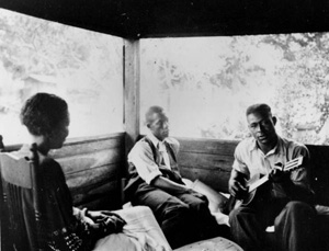 Gabriel Brown playing guitar as Rochelle French and Zora Neale Hurston listen: Eatonville, Florida