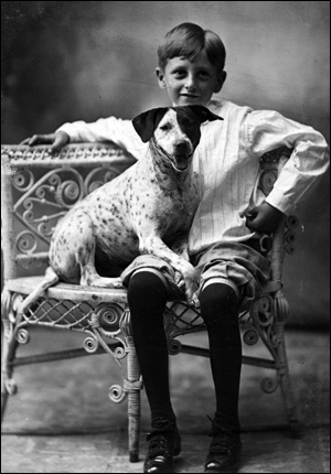 Boy posed with dog on wicker chair (191-)