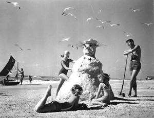 Three girls making a "sandman" at the beach (1964)