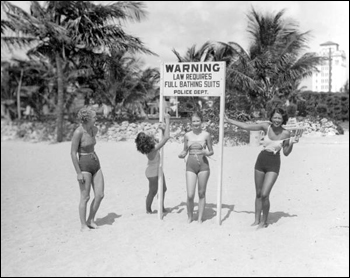 Young women making fun of sign at beach requiring full bathing suits: Miami, Florida (1934)