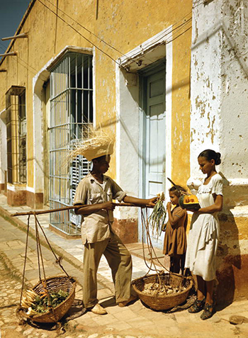 Street vendor holding out onions to a woman holding tropical fruit in Cuba