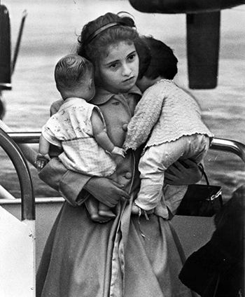 Young Cuban refugee holding her dolls in airport (1961)