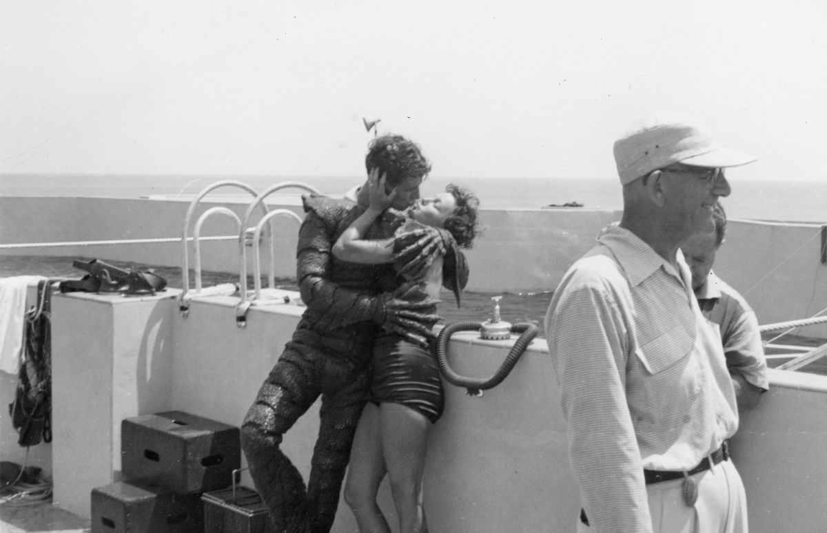 "Gill-man" Ricou Browning posing for a kiss with an unidentified woman on the set of "Revenge of the Creature" at Marine Studios.
