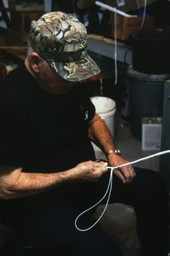 Close-up view showing whipmaker Ernest "Shelby" Braddock braiding a cow whip in the shop at his home in De Land, Florida.