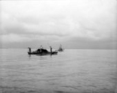 Three men "tonging" for oysters from barge.