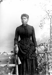 Woman in dark dress, holding a fan.