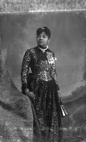 Woman in lace-overlay dress, holding a fan.