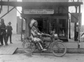 Indian on an Indian Powerplus motorcycle in front of C.T. Kruse's motorcyle shop