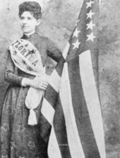 Mena E. Williams Hirschberg stands by a U.S. flag - Tallahassee, Florida.