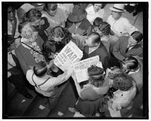 Crowd of people reading the front page of two newspapers, one with the headline War Bombs Rain on Warsaw and another that reads Poland Invaded Cities Bombed.