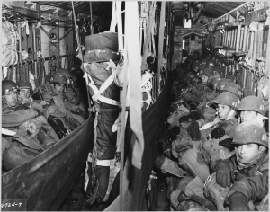 Paratroopers of the 187th Airborne Regimental Combat Team seated in the cargo compartment of a military transport aircraft.