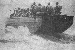 An amphibious vehicle in shallow water with soldiers facing away from the camera.