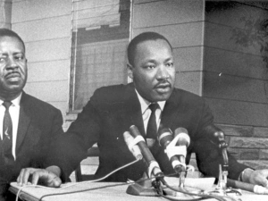 Still image taken from a Highway Patrol film showing Dr. Martin Luther King Jr. speaking at a podium with Ralph Abernathy standing beside him.
