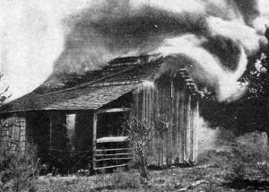 Deliberate burning of an African American home with heavy smoke rising from the wooden structure.