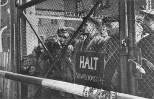 People imprisoned at the Auschwitz concentration camp standing behind a locked gate.